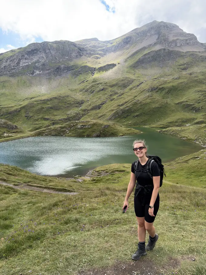 Rebecca mit Rucksack auf einer Wiese oberhalb des Bachalpsees, dahinter grüne Hänge und ein felsiger Gipfel