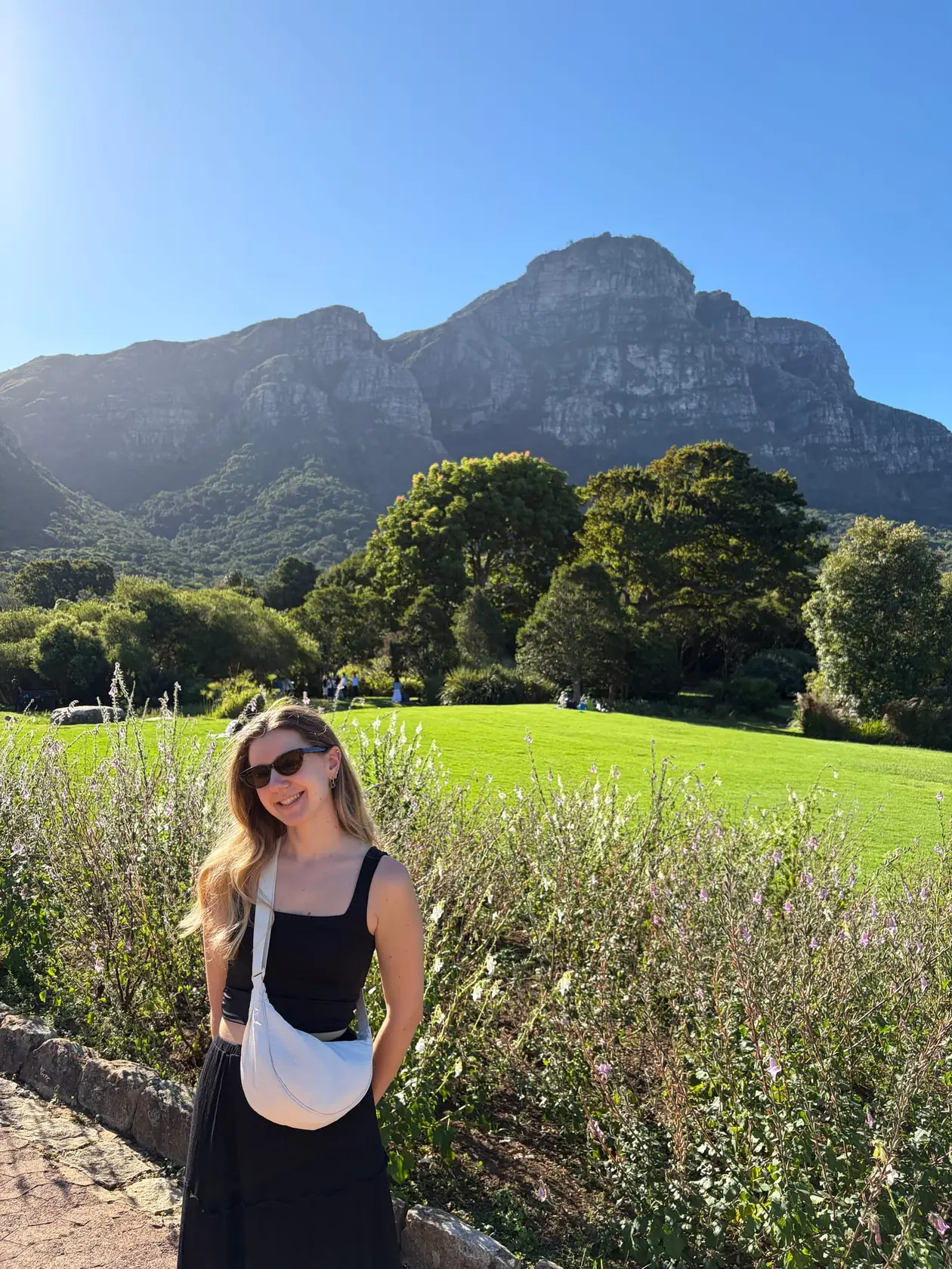 Rebecca steht lächelnd vor einem Teich im Kirstenbosch-Garten, im Hintergrund der Tafelberg