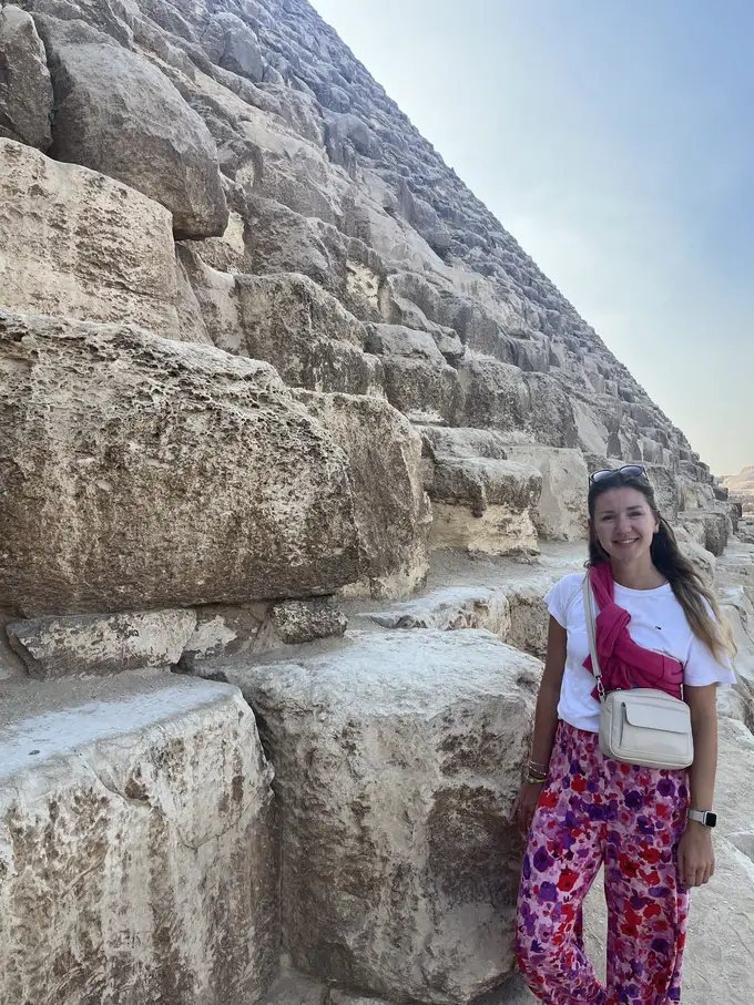 Rebecca steht lächelnd neben den unteren Steinblöcken einer Pyramide, die ihr bis über die Schulter reichen