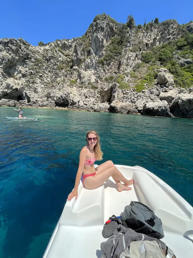 Rebecca sitzt vorn auf einem weißen Tretboot, dahinter tiefblaues Wasser und eine Felsküste