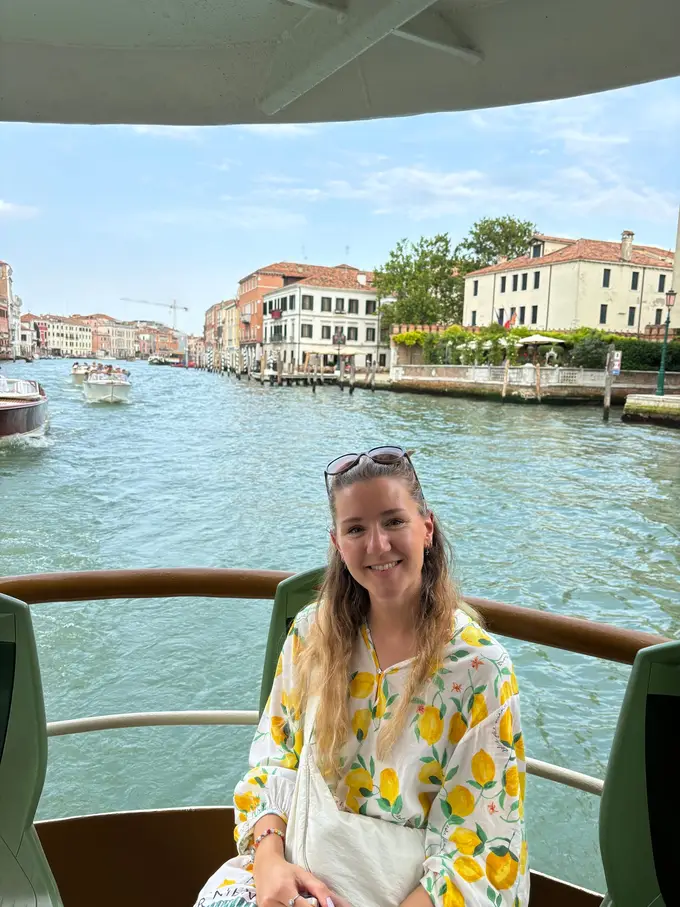 Rebecca sitzt lächelnd hinten auf einem Vaporetto, hinter ihr der Canal Grande mit Wassertaxis und Häusern am Ufer