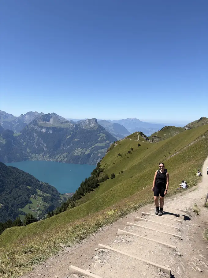Rebecca kommt Holzstufen auf dem Grat herauf, dahinter ein See tief im Tal und Bergketten