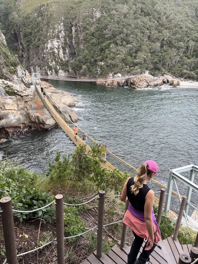 Rebecca geht mit pinker Kappe über die Hängebrücke, unten fließt der Storms River ins Meer