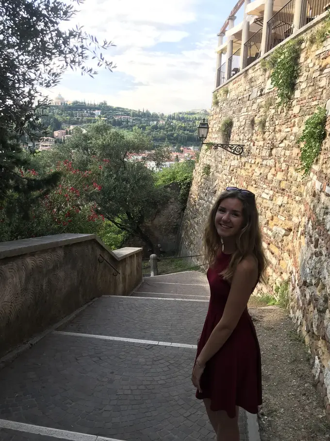 Rebecca im roten Kleid auf einer Steintreppe zwischen einer Mauer und Grün