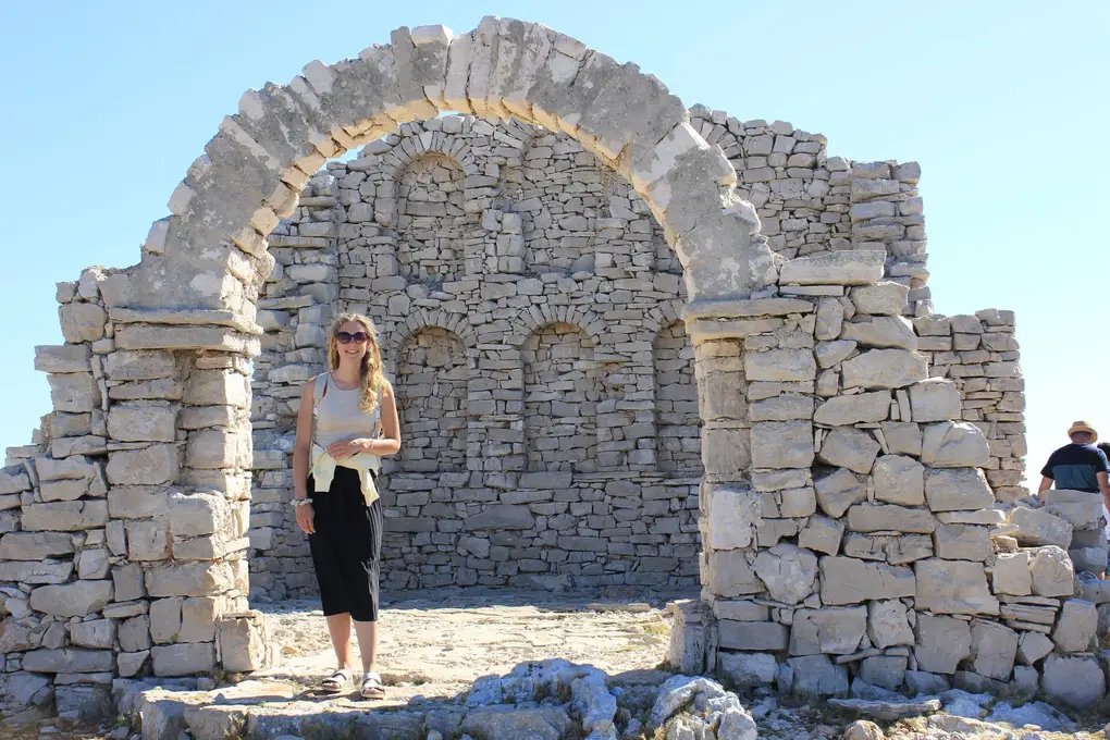 Rebecca steht unter einem großen Bogen einer Ruine aus Trockenstein, am Rand ein Mann mit Hut