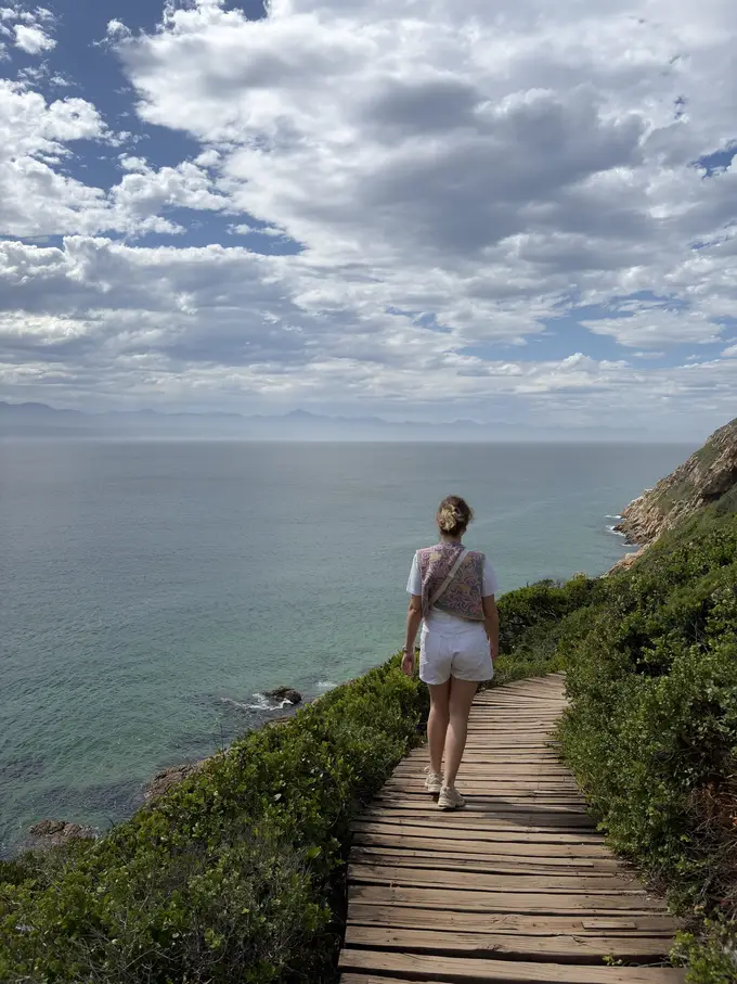 Rebecca geht auf einem Holzsteg über den Felsrücken von Robberg, das Meer auf beiden Seiten