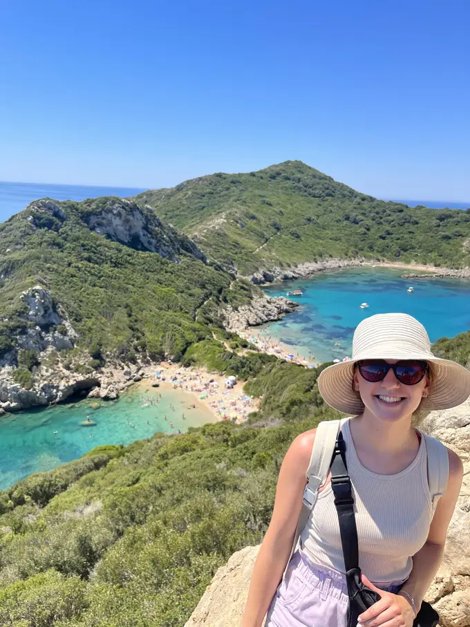 Rebecca mit Sonnenhut und Sonnenbrille, hinter ihr unten die zwei Buchten von Porto Timoni