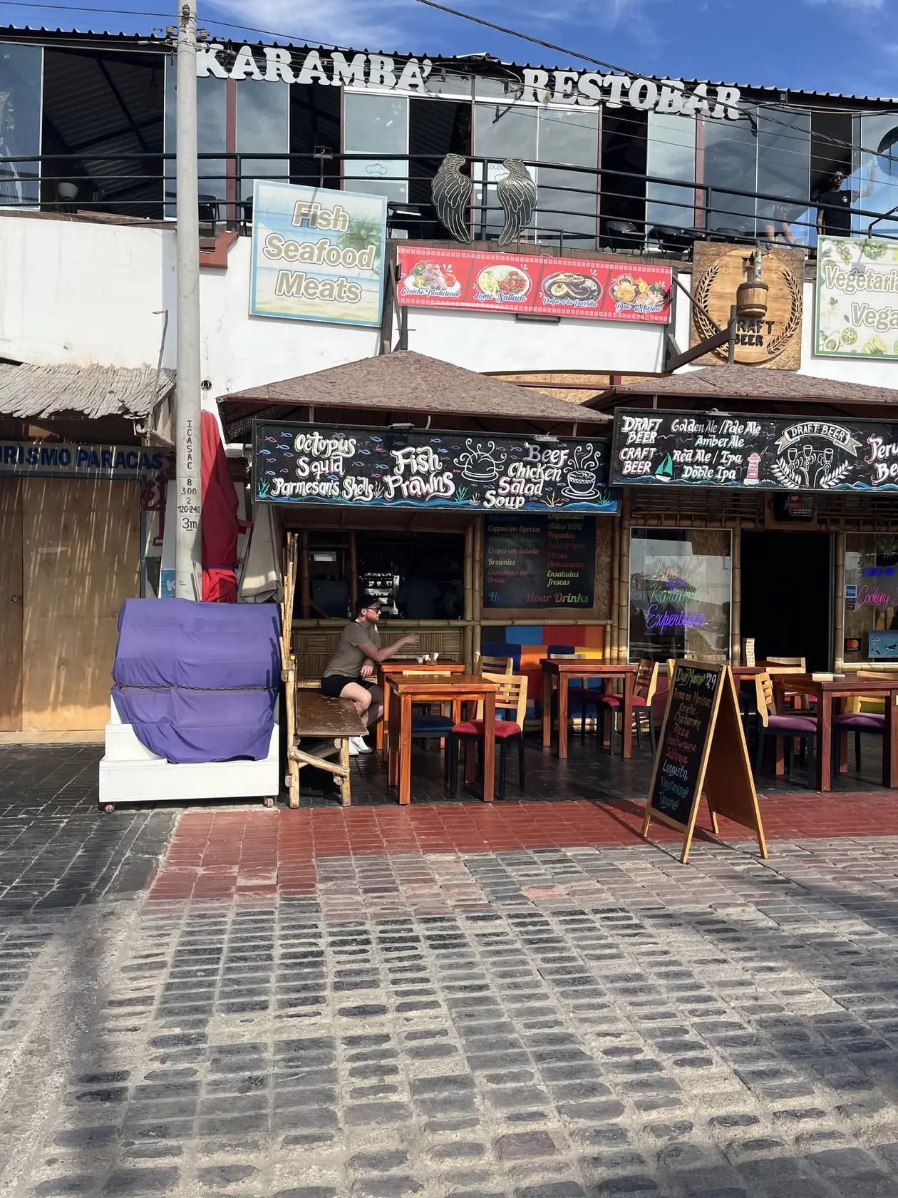Holzfassade eines Restaurants an der Uferpromenade mit Tafeln für Fisch und Meeresfrüchte, davor Tische und ein Aufsteller