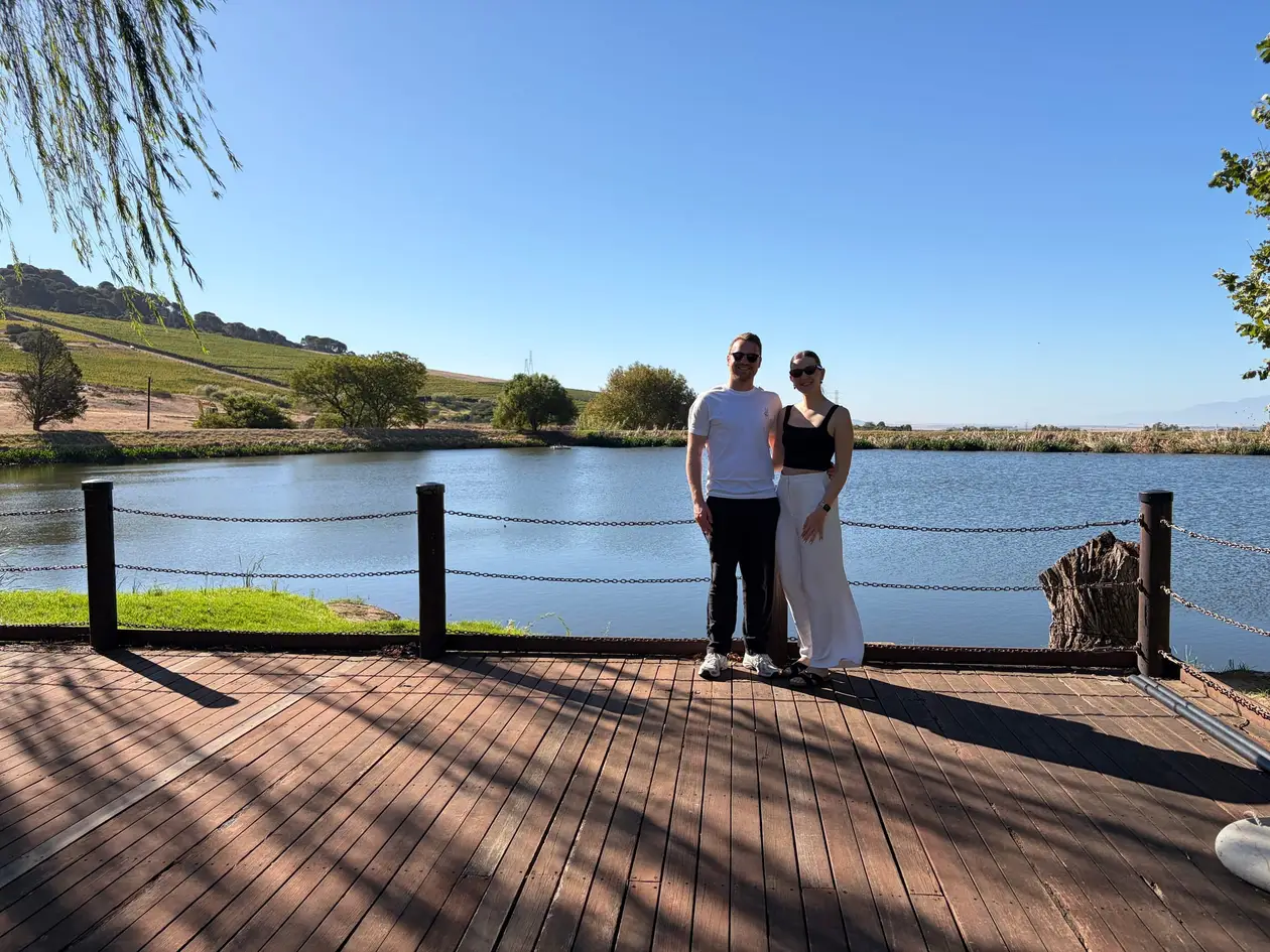 Max und Rebecca stehen auf einer Holzterrasse an einem See auf dem Weingut Rhebokskloof