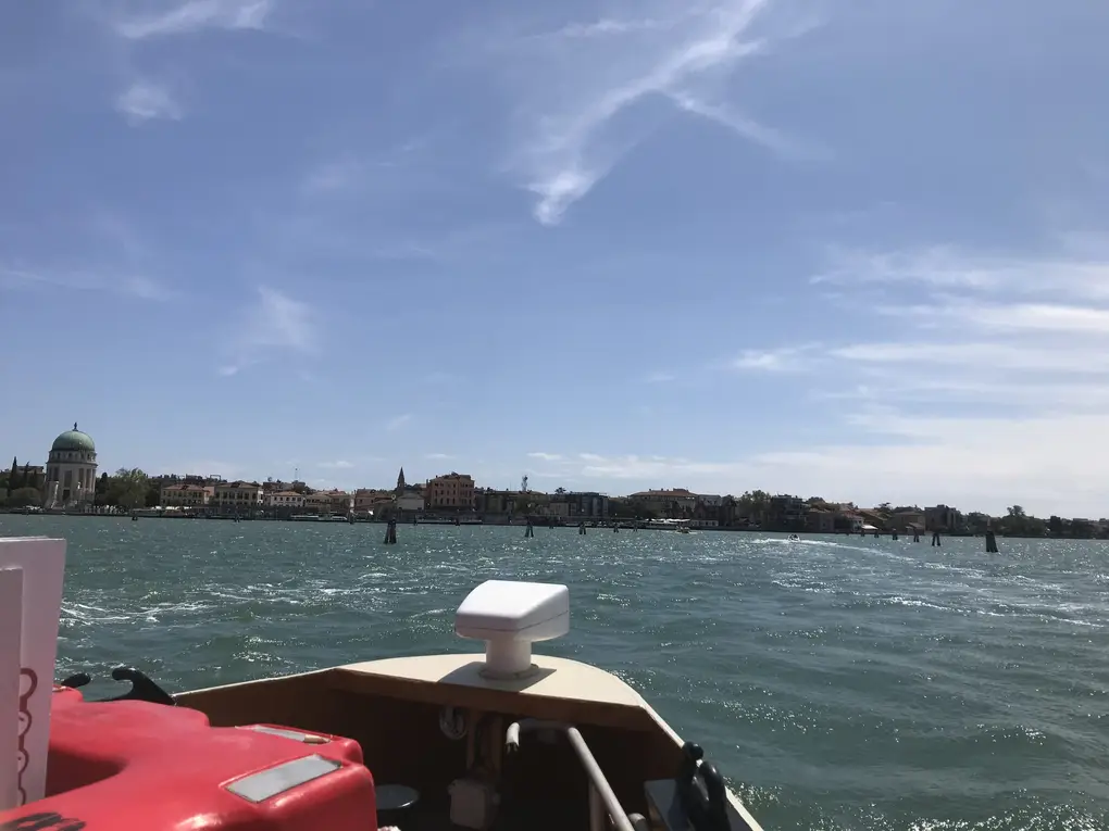 Blick über den Bug eines Boots auf offenes Wasser und einen flachen Inselstreifen