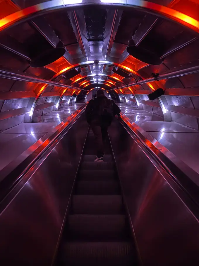 Lange Rolltreppe in einer Röhre des Atomiums, rot und weiß beleuchtet, oben fährt eine Person