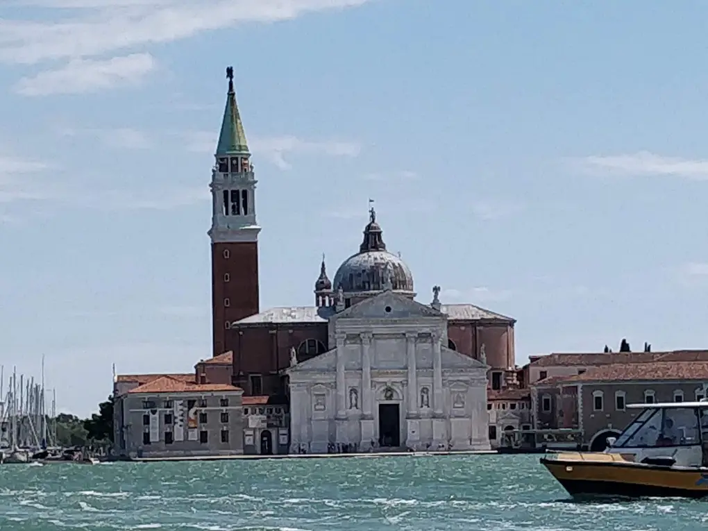 Die Kirche San Giorgio Maggiore mit Kuppel und rotem Glockenturm auf ihrer Insel, davor Wasser und ein Motorboot