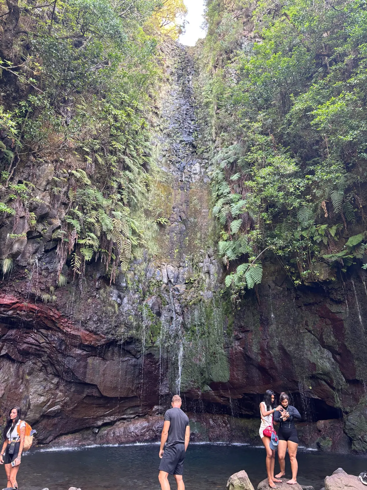 Mehrere Personen stehen nacheinander im Becken unter einem schmalen Wasserfall