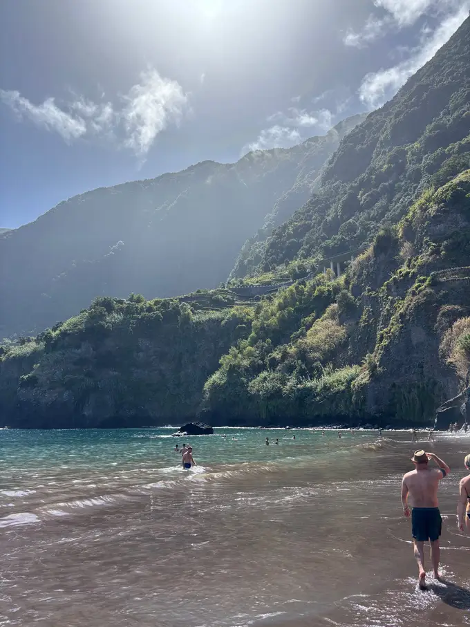 Mehrere Personen stehen und schwimmen im Wasser einer Bucht, umgeben von steilen bewaldeten Hängen