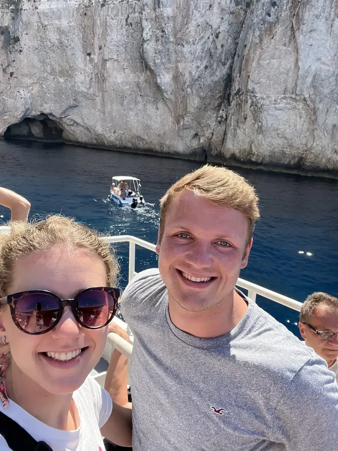 Selfie von Rebecca und Max an der Reling, hinter ihnen eine Felswand und ein kleines Motorboot