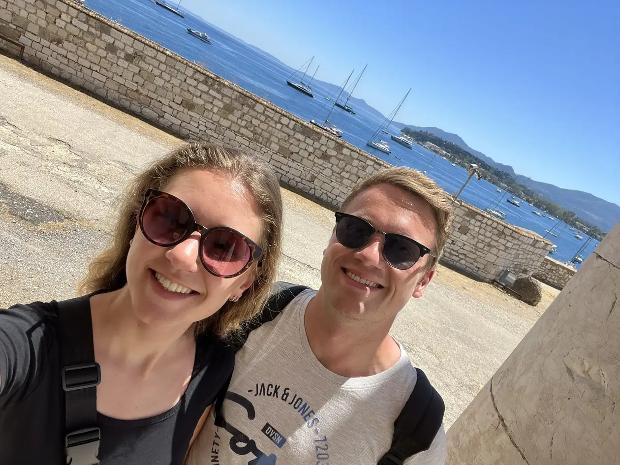 Selfie von Rebecca und Max auf der Festung, hinter ihnen eine Mauer und Segelboote in der Bucht