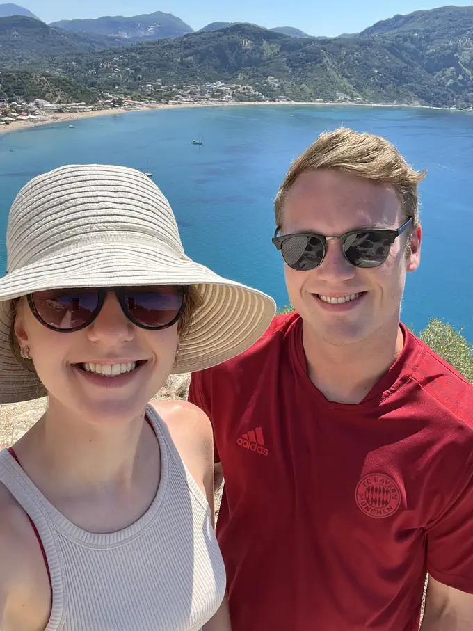 Selfie von Rebecca mit Sonnenhut und Max, hinter ihnen tief unten eine Bucht mit Sandstrand