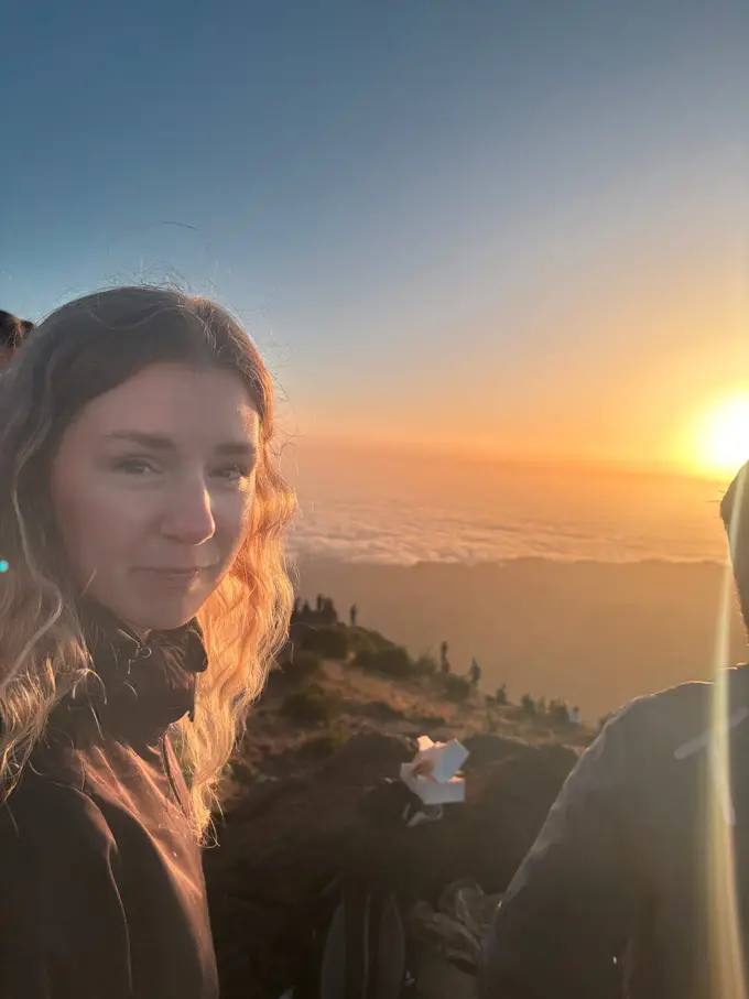 Nahaufnahme von Rebecca beim Selfie, im Hintergrund geht die Sonne über dem Wolkenmeer auf