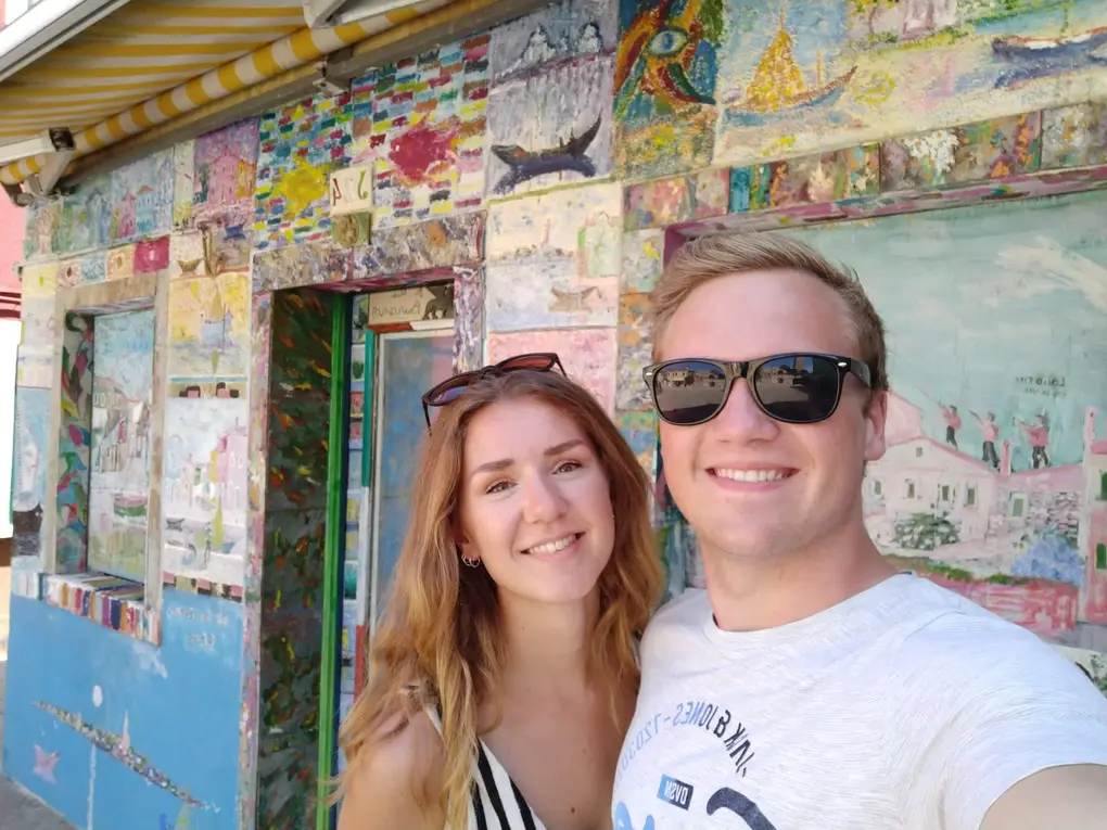 Selfie von Rebecca und Max vor einer Hauswand, die über und über mit bunten Bildern bemalt ist