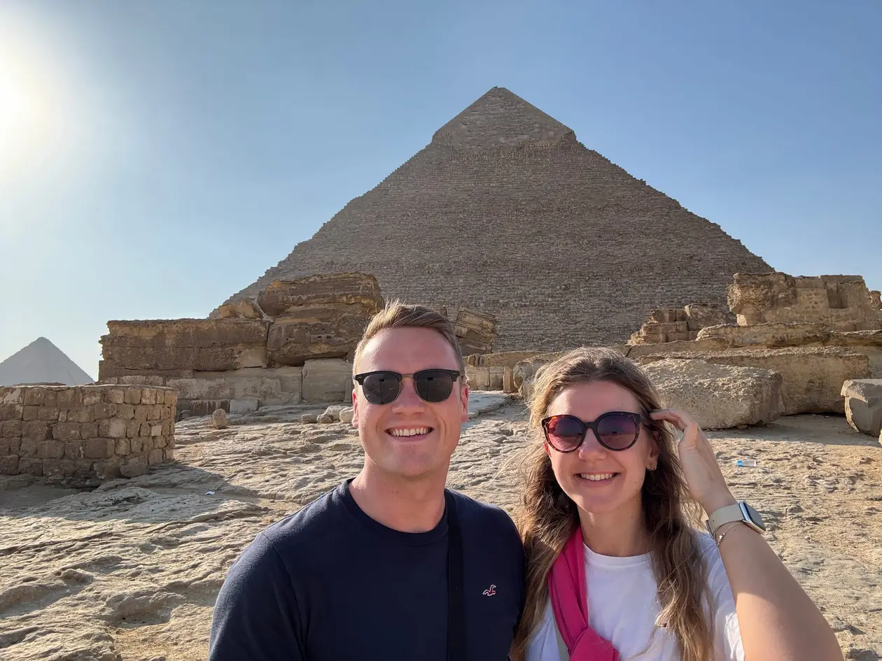 Selfie von Max und Rebecca mit Sonnenbrillen vor einer Pyramide, deren Spitze noch Reste der glatten Verkleidung trägt, davor Mauerreste und Steinblöcke