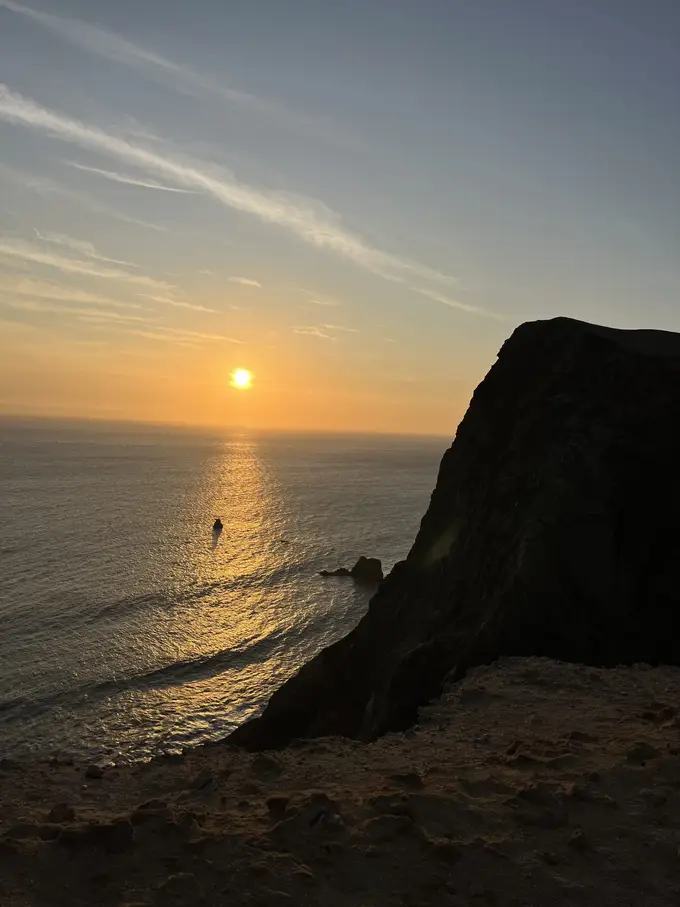Die tief stehende Sonne spiegelt sich im Pazifik, rechts ragt eine dunkle Klippe ins Bild