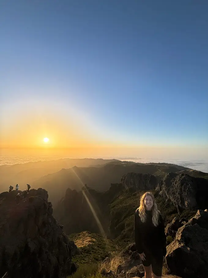 Die Sonne geht über einem felsigen Grat auf, eine Person steht als Silhouette am Rand