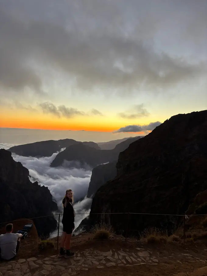 Oranger Abendhimmel über dem Wolkenmeer, eine Person steht am Rand des Aussichtspunkts