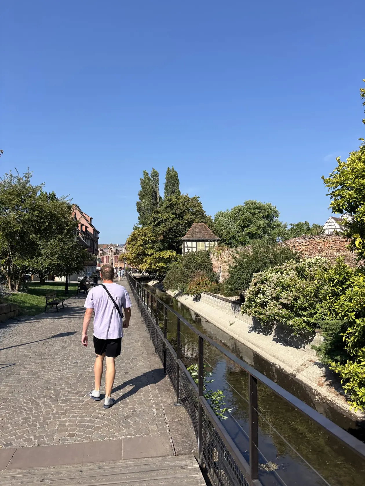 Ein Mann in lila T-Shirt läuft auf einem gepflasterten Weg an einem schmalen Kanal entlang, daneben eine Backsteinmauer und ein kleines Fachwerkhaus