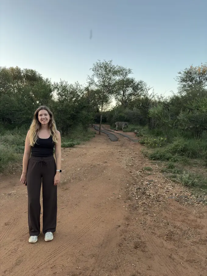 Rebecca geht einen sandigen Weg durchs Buschland im Dämmerlicht