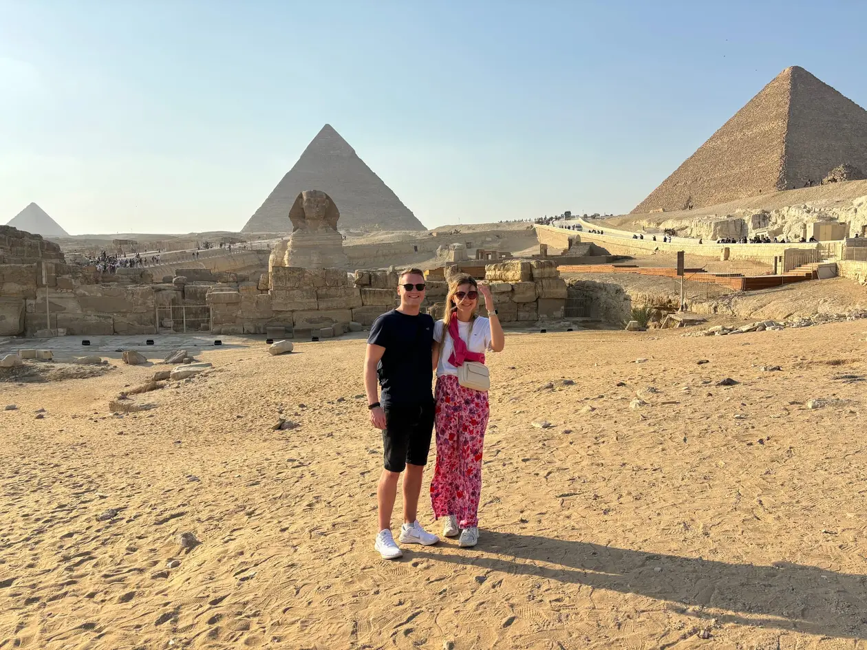 Max und Rebecca stehen im Sand vor der Sphinx, dahinter drei Pyramiden, eine davon groß am rechten Bildrand