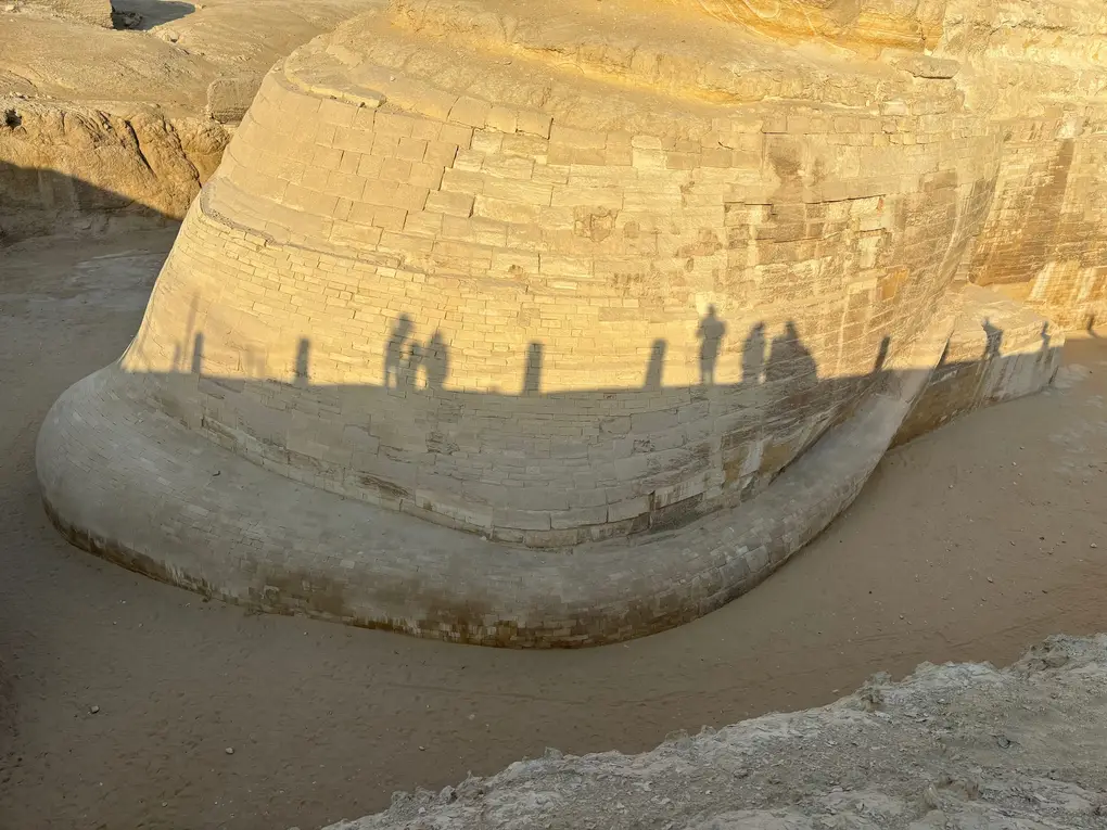 Blick von oben auf die gemauerte Flanke der Sphinx, darauf die Schatten der Besucher, die am Rand der Grube stehen