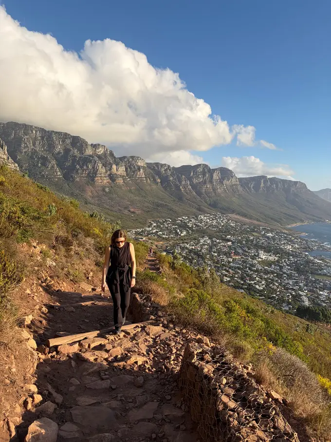 Eine Person geht einen schmalen Pfad hinauf, der sich um den Lion's Head windet, unten breitet sich Kapstadt aus