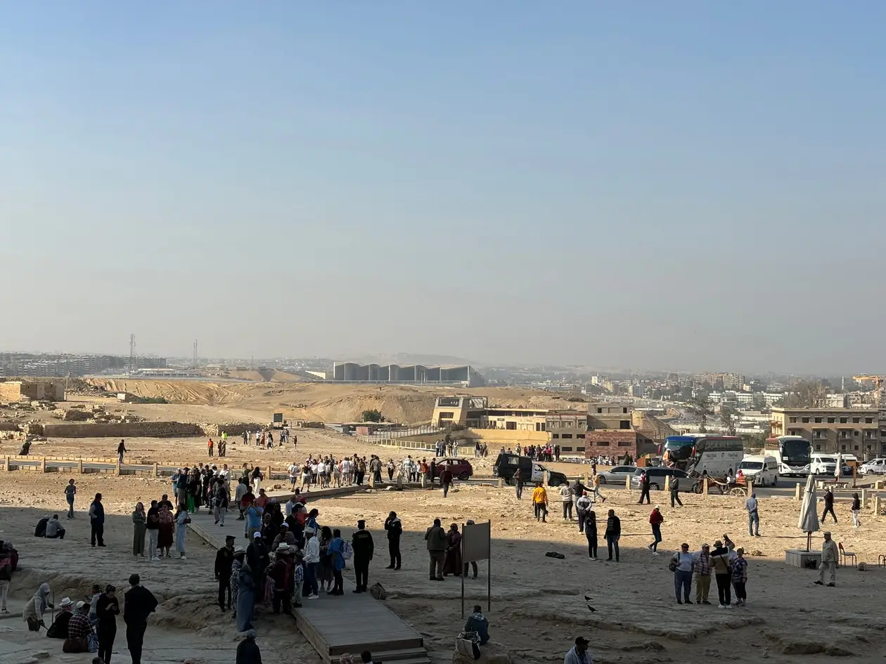 Blick vom Plateau über Besuchergruppen, einen Holzsteg, Reisebusse und Parkplätze auf die Stadt, die direkt dahinter beginnt