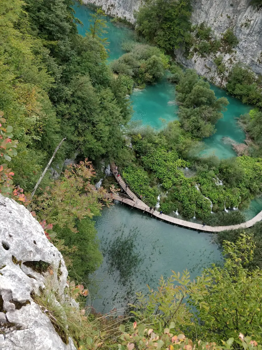 Steiler Blick von oben auf Holzstege mit Besuchern zwischen türkisen Becken und kleinen Wasserfällen