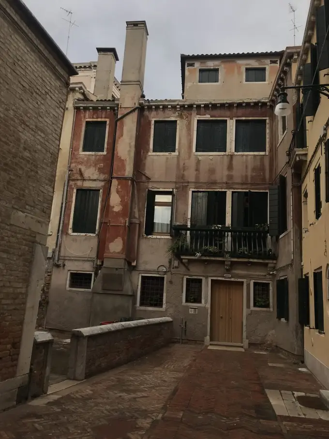 Ein stiller Hof vor einem verwitterten Haus mit grünen Fensterläden