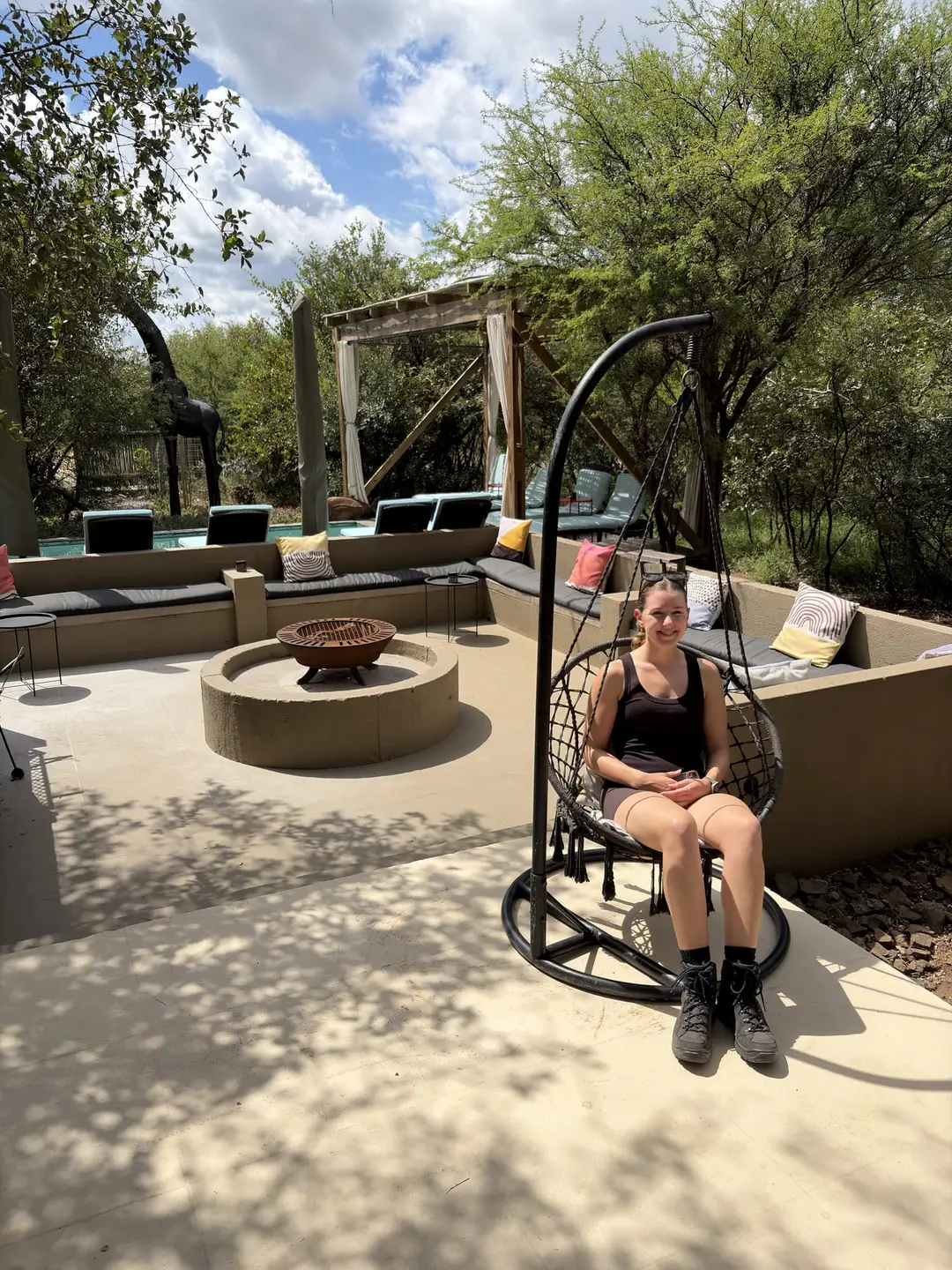 Rebecca sitzt in einem Hängesessel auf der überdachten Terrasse der Lodge, daneben eine Feuerstelle