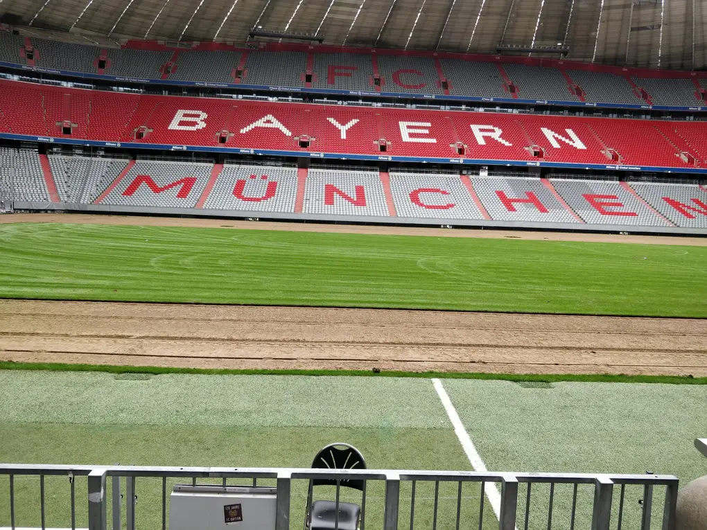 Blick vom Spielfeldrand über den Rasen auf die leere Tribüne, in deren Sitzen in großen Buchstaben FC Bayern München steht