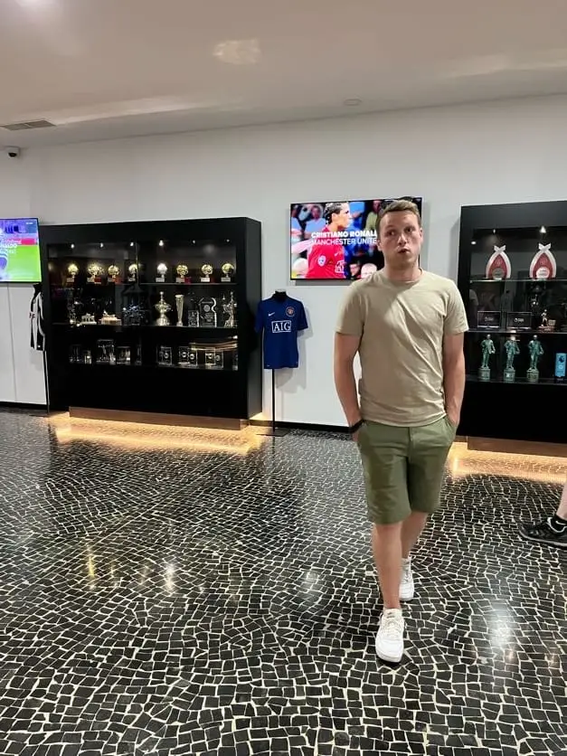 Mann steht in einem Museumsraum zwischen Vitrinen mit Pokalen und einem Trikot