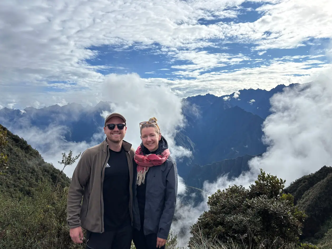 Max und Rebecca mit Sonnenbrillen auf einem Grat, hinter ihnen quellen Wolken aus den Tälern zwischen dunklen Bergen