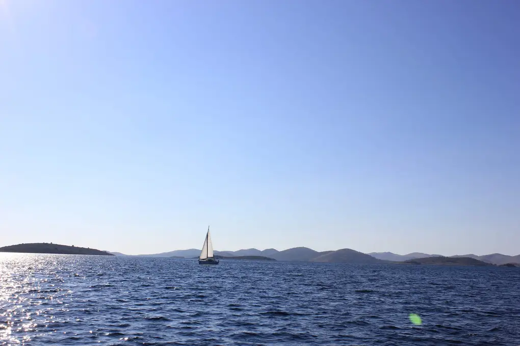 Offenes Meer mit einem Segelboot, am Horizont eine Kette flacher Inseln