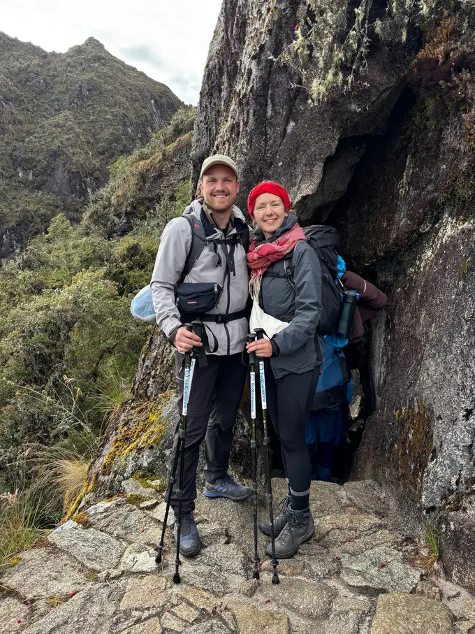 Max und Rebecca auf gepflastertem Weg vor einem Durchgang im Fels, rundherum Moos und dichter Bergwald
