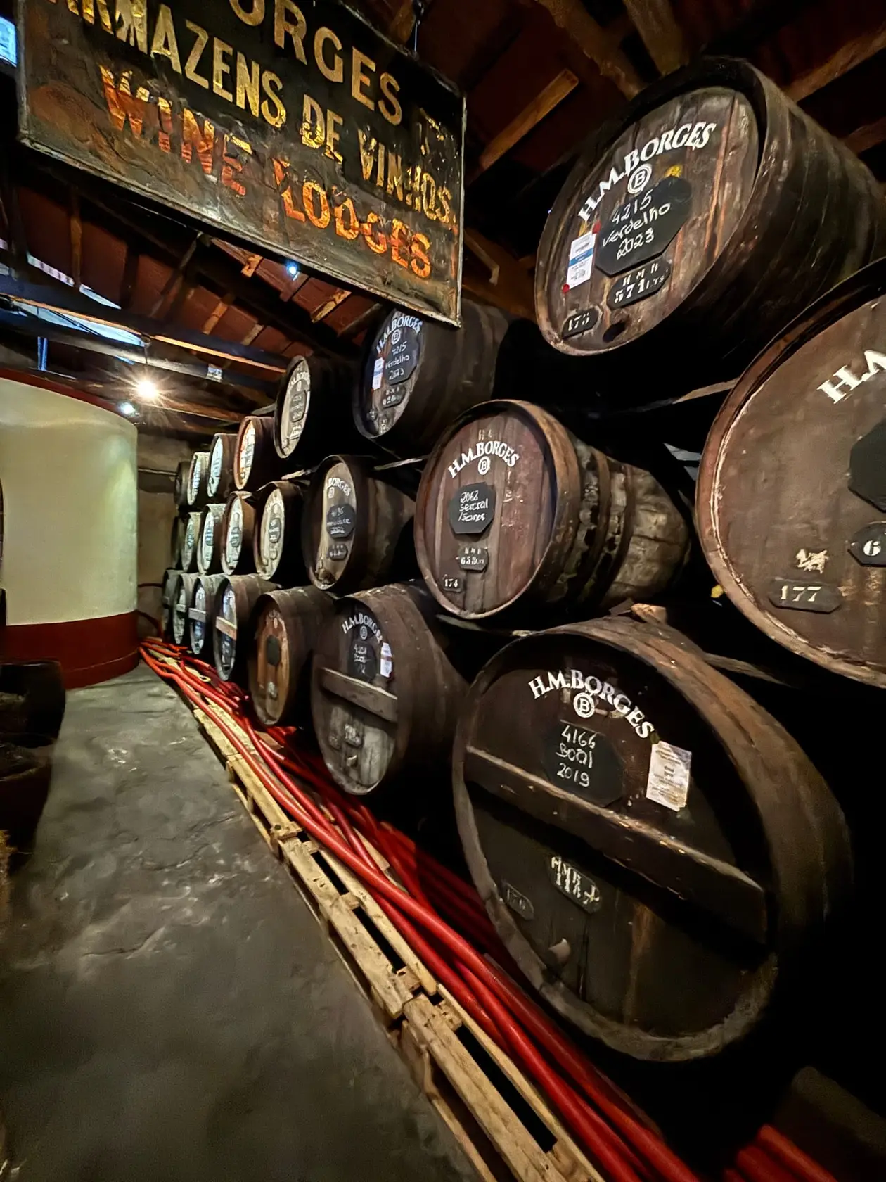 Lagerhalle mit aufgestapelten Holzfässern und Schild „Armazéns de Vinhos Wine Lodges“