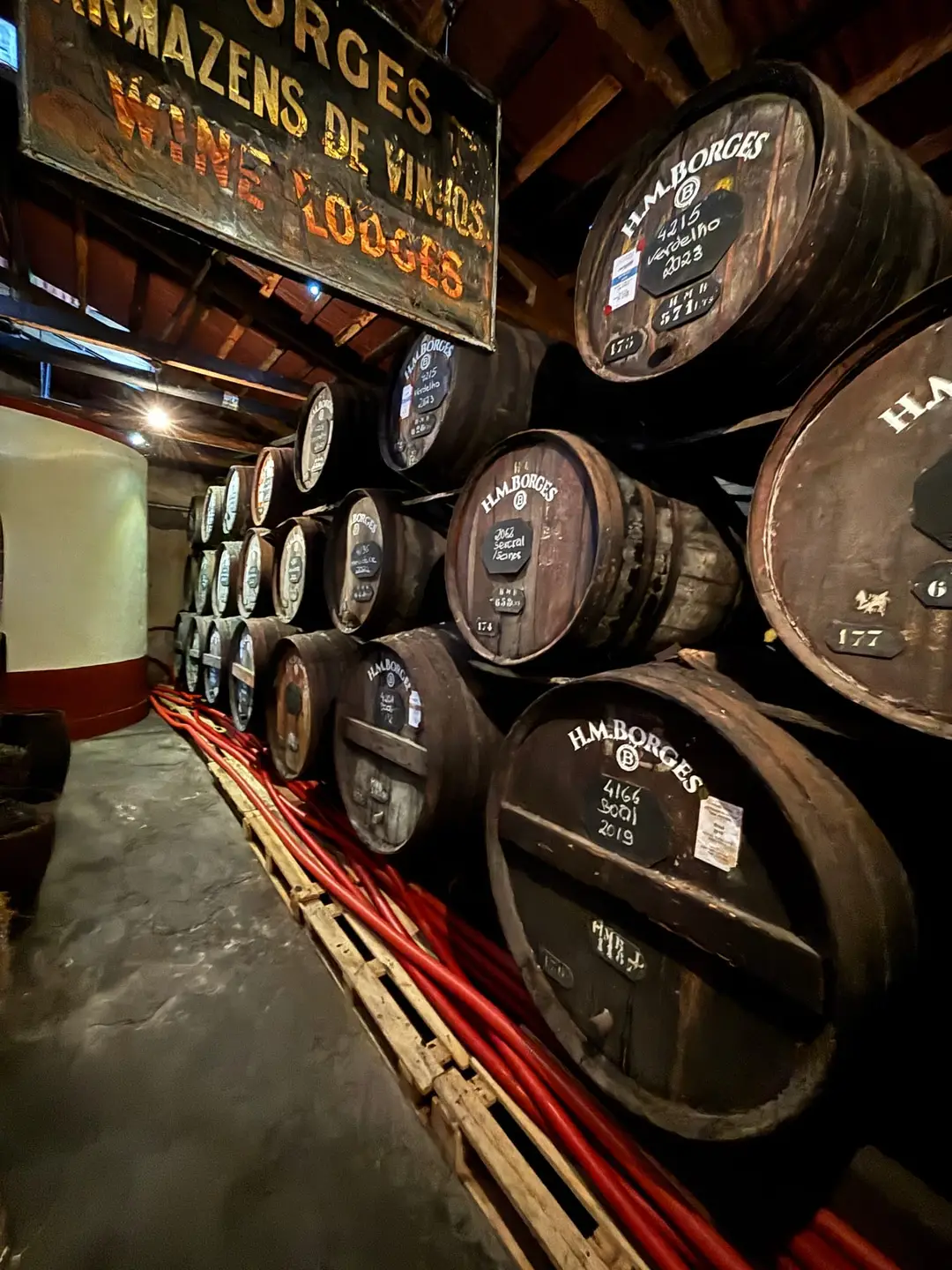 Lagerhalle mit aufgestapelten Holzfässern und Schild „Armazéns de Vinhos Wine Lodges“