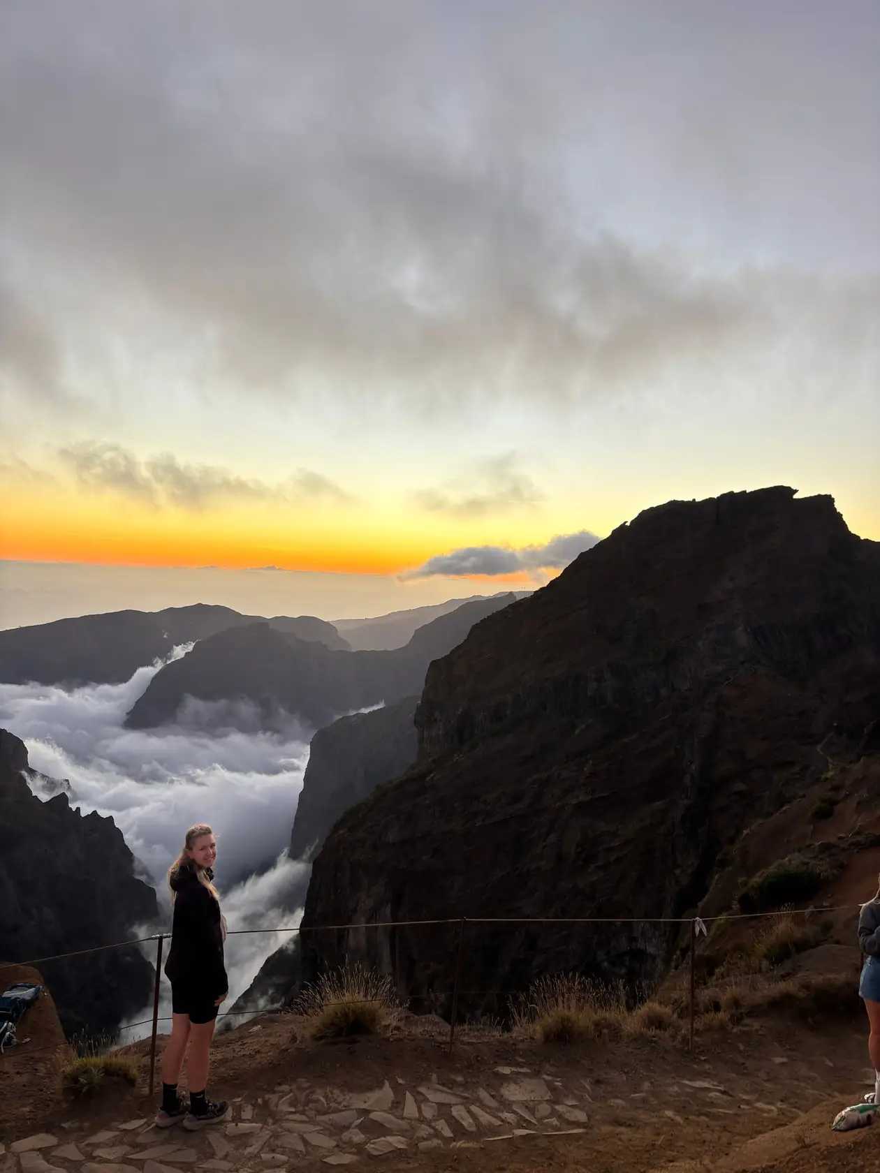 Oranger Abendhimmel über dem Wolkenmeer, eine Person steht am Aussichtspunkt