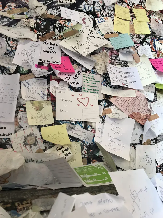 Nahaufnahme einer Wand voller handbeschriebener Zettel mit Namen und Herzen