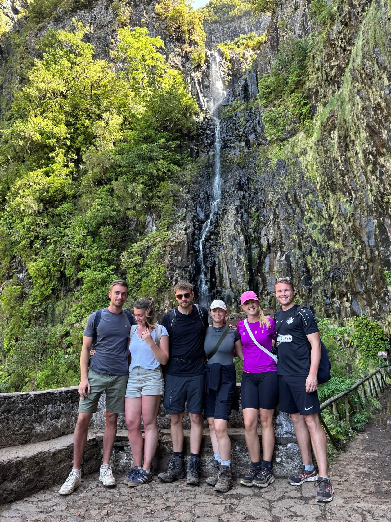 Sechs Personen posieren lächelnd vor einem schmalen, hohen Wasserfall in einer Felsschlucht